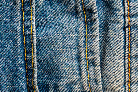 Blue jeans fabric background or denim texture with seam. Close up view