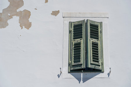 Window with green wooden shutters on old white stucco wall and copy space, Europe, close upの写真素材