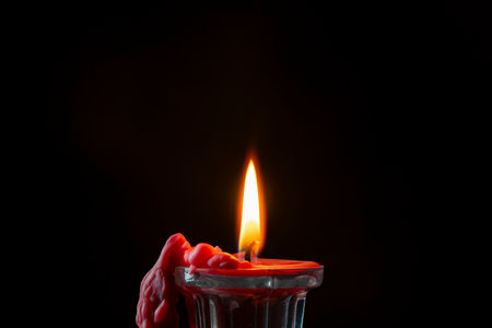 Glass candlestick with red burning candle on black background, close up