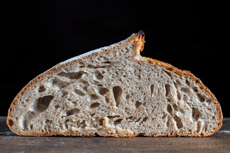 Half round loaf of freshly baked sourdough bread on wooden cutting board, close up. Rustic sourdough bread. Cooking healthy sourdough bread at homeの写真素材