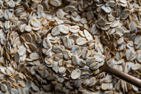 Dry oat flakes in a metal spoon, top view on uncooked raw oat grains background. Healthy breakfast and diet eating ingredients for making oatmeal porridge. Gastronomy concept, organic foodの写真素材