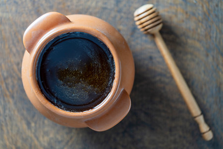 Raw honey in a ceramic jar and honey dipper on the wooden background, close up, top viewの写真素材