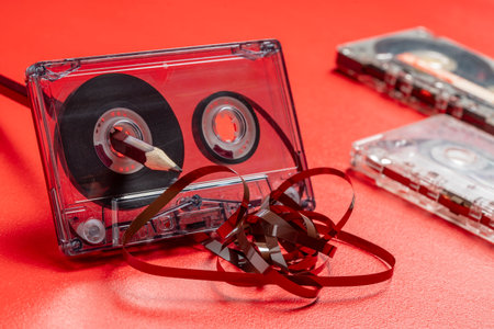 Rewinding magnetic tape in a cassette manually with a pencil on a red background, close up. Old methods of rewinding music tapes, vintage styleの写真素材