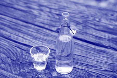Bottle and glass with water on the wooden table, close up. Trendy color of the picture