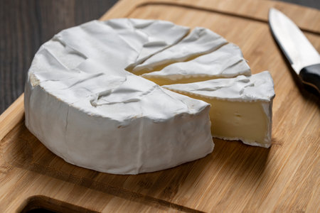 Cutting of white soft moldy Camembert cheese on a wooden cutting board with knife , close upの写真素材