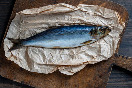Fresh raw whole fish herring on parchment paper on wooden cutting board, top view, close upの写真素材