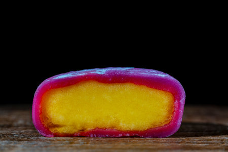 Pink mochi ice cream with yellow tropical fruit filling on wooden table on black background, close up. Traditional Japanese mochi is an unusual dessert that resembles both a cake and ice creamの写真素材