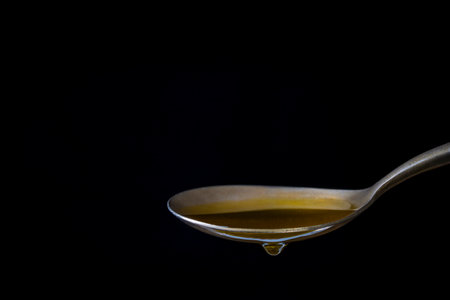 Metal spoon with extra virgin olive oil on black background, close upの写真素材