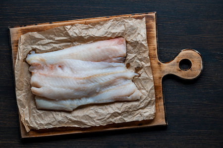 Raw Hake fish fillets in a wooden tray with herbs. black background. top view.