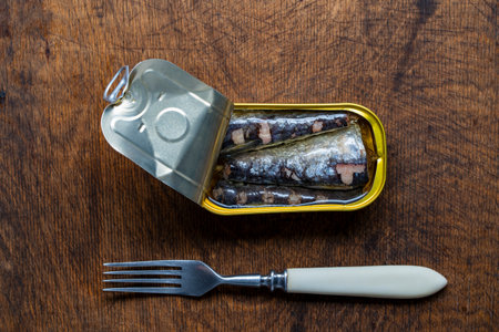 Open tin can of sardine fish and fork on wooden table background, close up, top viewの写真素材