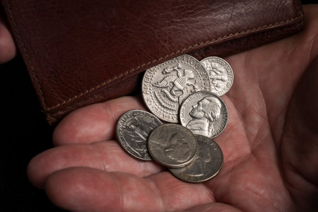 Old poor man's hand shakes out American cents coins from a leather wallet, close up. Inflation,...