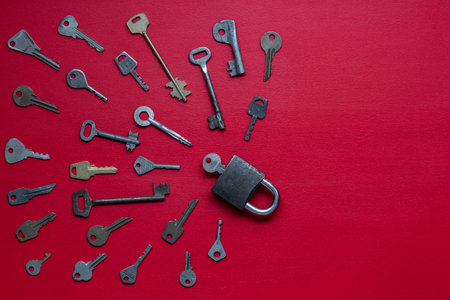 One lock and many different old keys on red background, top view, close up.の写真素材