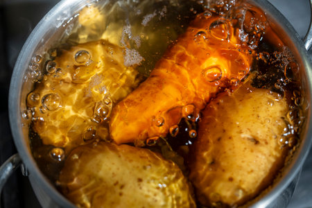 Saucepan with potatoes in skins and carrots in boiling water on a gas stove, close upの写真素材