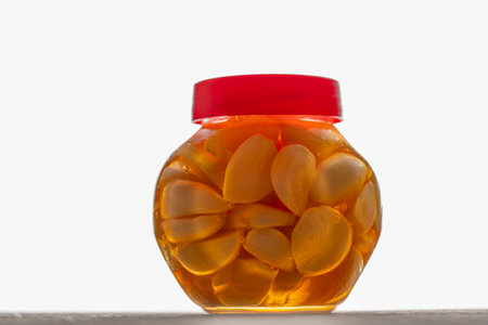 Sliced garlic cloves in honey in glass jar on a white background, close up.の写真素材
