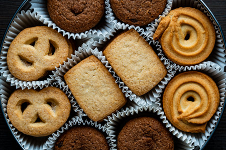 Crispy crumbly shortbread cookies in a round metal box on wooden table, top view, close up