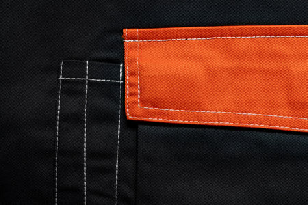 Orange flap of black pants pocket, close up. Background and texture of fabric