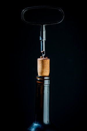 Opening a glass wine bottle with corkscrew on black background, close up