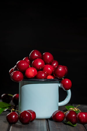 Tasty ripe red cherries in a metal blue mug on a wooden table. Fresh sweet cherry, close upの写真素材