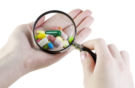 hand with a magnifying glass looking at pillsの写真素材