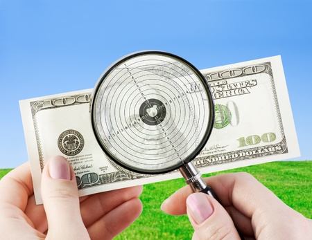 hands using a magnifying glass to see US dollar bill の写真素材