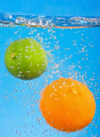 citrus fruits fall into the water on a blue backgroundの写真素材