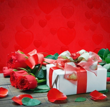 fresh red roses and a gift isolated on a red background with heartsの写真素材
