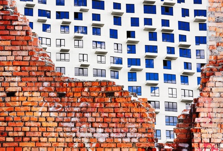old destroyed brick wall of the building and a new house under constructionの写真素材