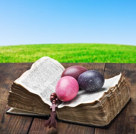 decorated with painted Easter eggs and an open bible wooden tableの写真素材