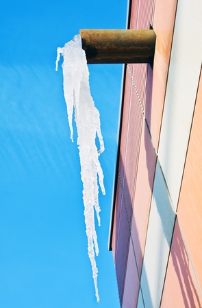 large icicle hanging from the roof of the winter against the blue skyの写真素材