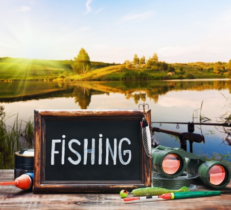 fishing tackle and a blackboard on a background of lake at sunsetの写真素材