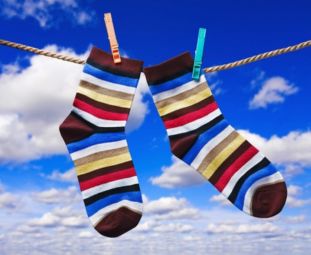 colorful socks hanging on clothespins against the sky with cloudsの写真素材
