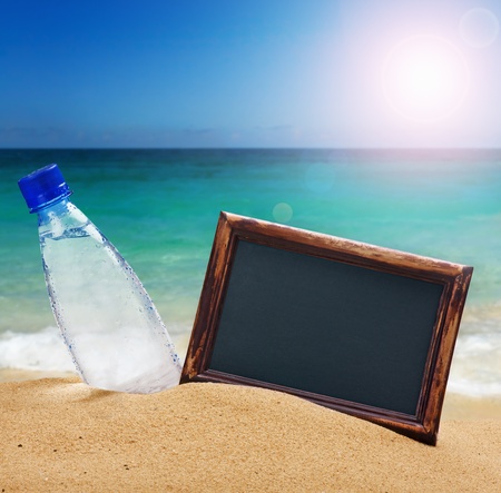 black board for the text and a bottle of water on the sandの写真素材