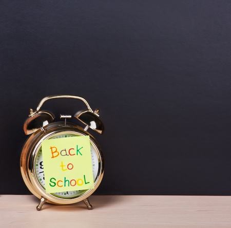 alarm clock and sticker with text back to school on the school board backgroundの写真素材