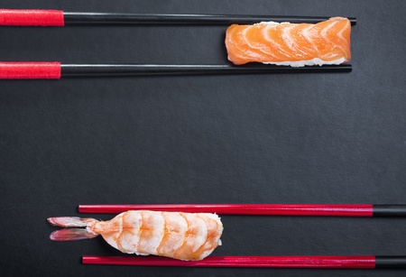 close-up of chopsticks and two sushi with salmon and shrimp on a black backgroundの写真素材