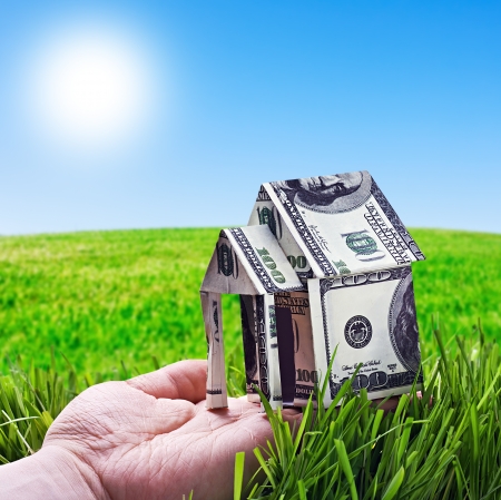 House made of money in hand on background of green fieldの写真素材