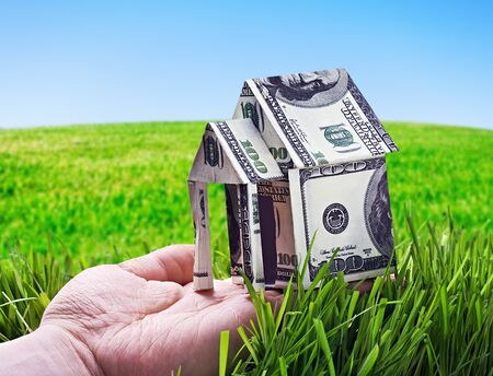 House made of money in hand on background of green fieldの写真素材