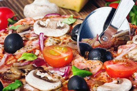 cutter cuts a fresh pizza with mushrooms and cheeseの写真素材