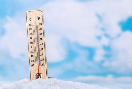 Thermometer in snow against the sky with clouds