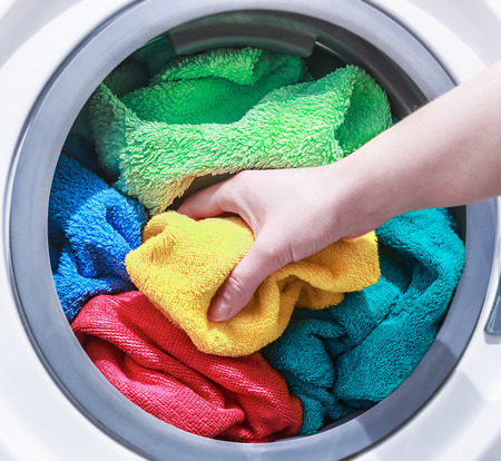 hand and puts the laundry into the washing machine. focus on a colored towelの写真素材