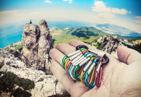 colorful carabiner climbing on a palm on a background of mountains. Focus on carbines. toned imageの写真素材