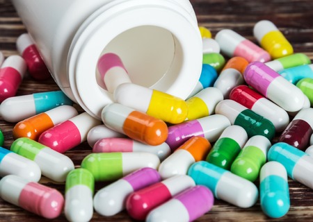 various colored pills and a vial of medication on a wooden table
