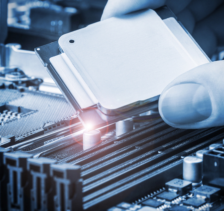 hand holding a CPU and inserts it into the motherboard. focus on cpu. Toned image
