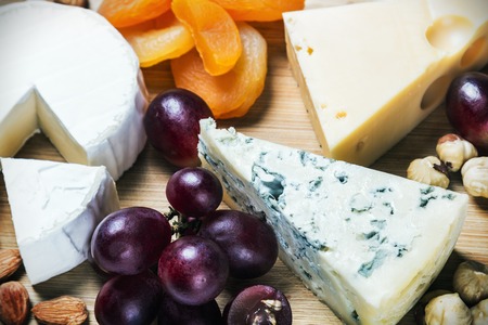 assorted cheeses, nuts and grapes on a wooden tableの写真素材