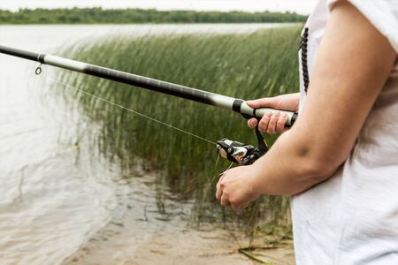 female hands holding a fishing rod and twist the handle of the fishing reel. Shallow depth of field, soft focusの写真素材