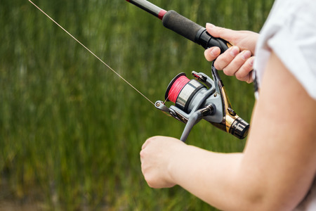 female hands holding a fishing rod feeder, and rotate the fishing reel. Shallow depth of field, soft...