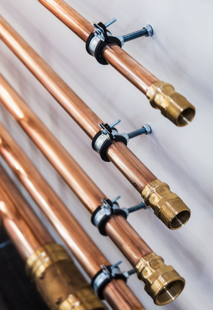 copper pipes and fittings for carrying out plumbing. Copper pipe in front of a white wallの写真素材
