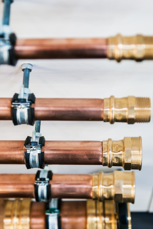 copper pipes and fittings for carrying out plumbing. Copper pipe in front of a white wallの写真素材