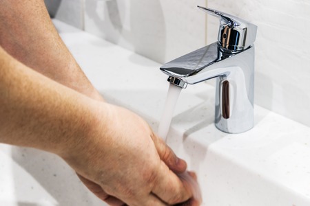 water faucet in the bathroom or toilet. water flows from the tap into male hands. Hands blurredの写真素材