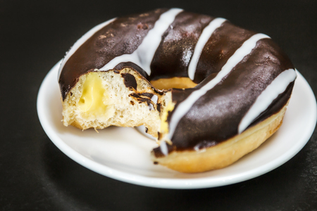 donut bitten covered with chocolate icing on a plateの写真素材