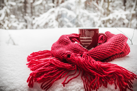 Cup with two hearts and a hot drink wrapped in a scarf in the snow. Concept for Valentine's dayの写真素材
